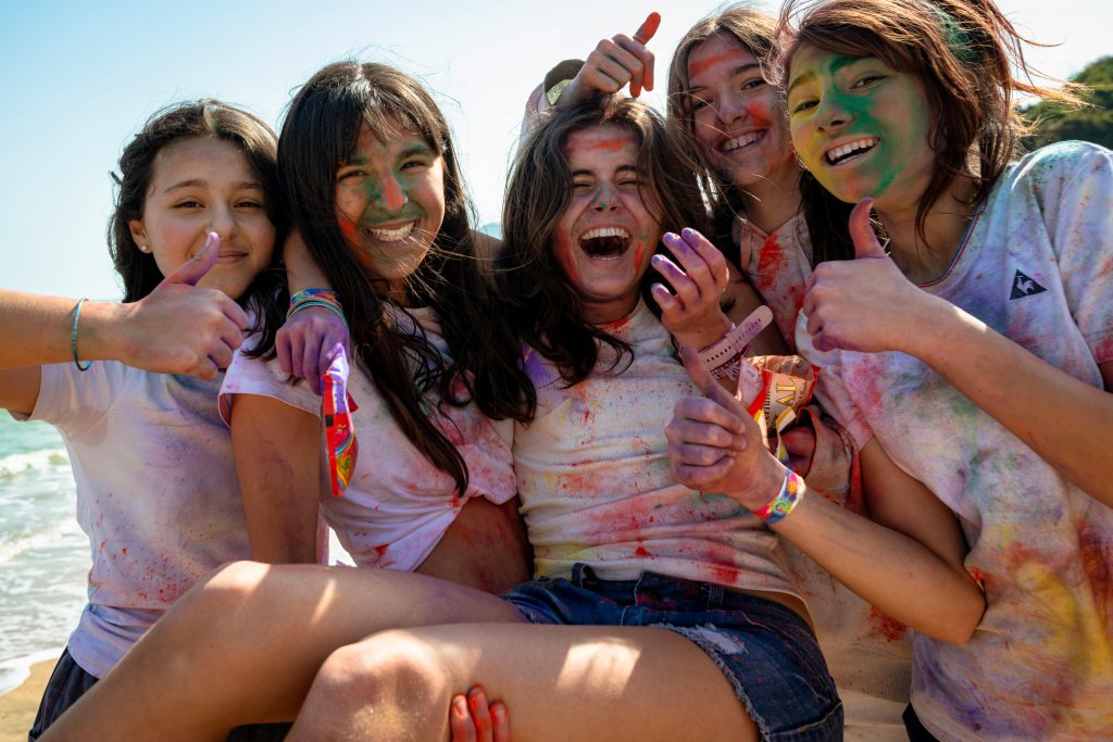 Joyful teenagers with colorful powder on a sunny beach day, expressing happiness and friendship.